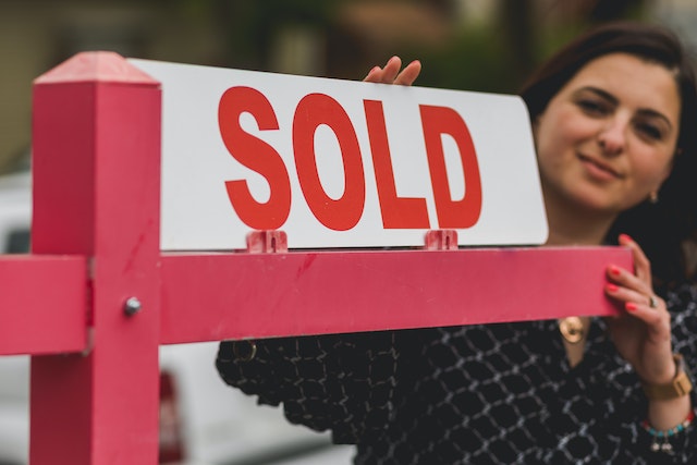 real estate agent placing a "SOLD" sign on a red signpost