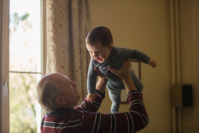 An older man in a red striped shirt lifting a baby into the air