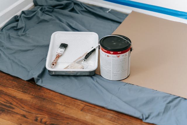 a can of paint, a paint tray, and a drop cloth on a wooden floor