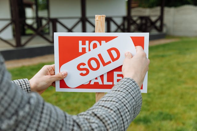 someone putting a "sold" sticker over a "home for sale" sign in a front lawn